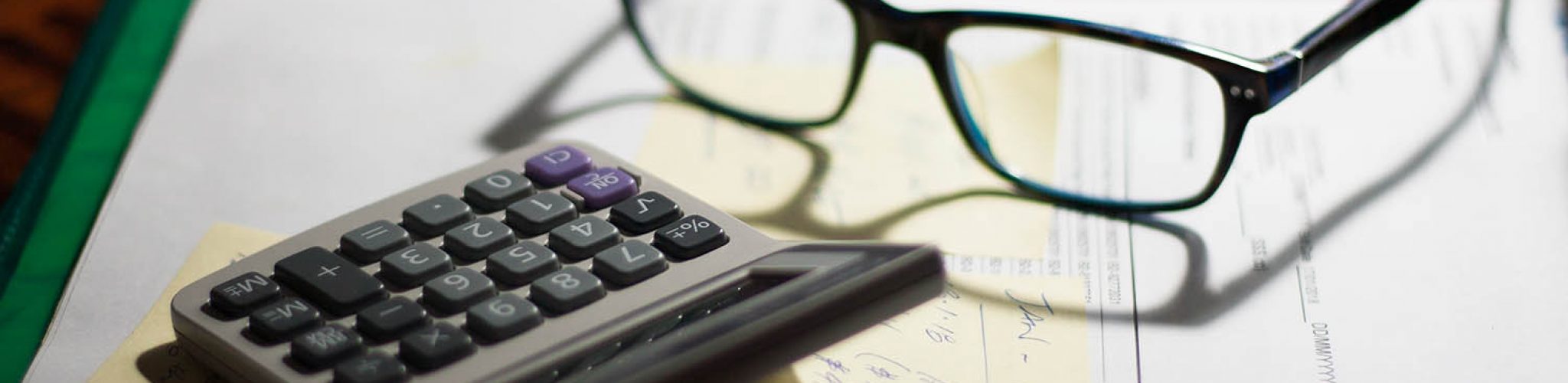 Glasses and calculator on a folder with documents, bills and notes on a desk